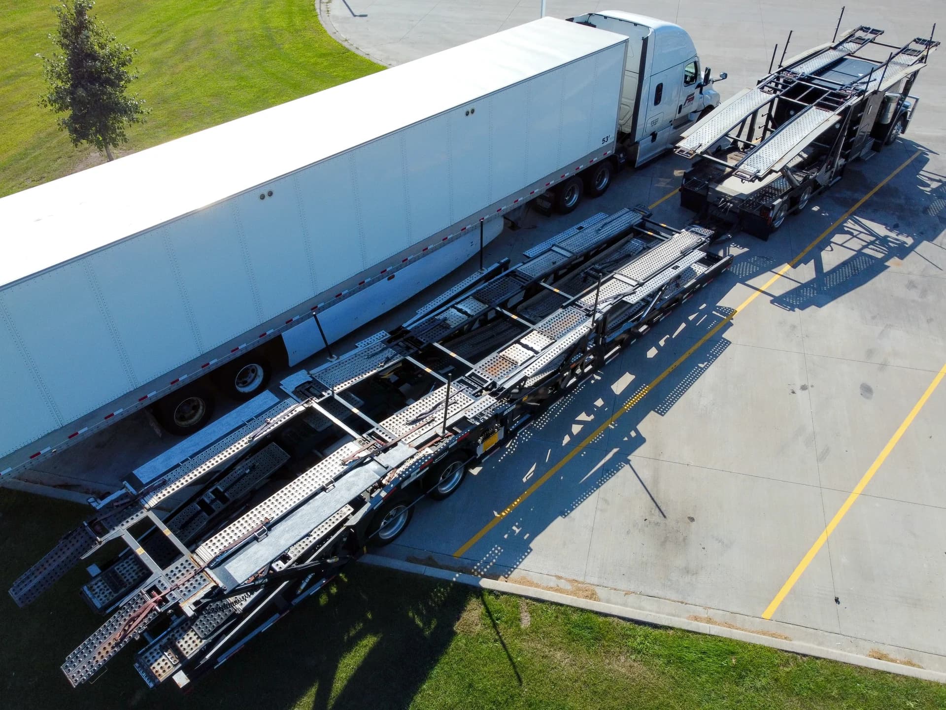 Open dual-axle car transporter trailer with wheel tracks and rear ramps